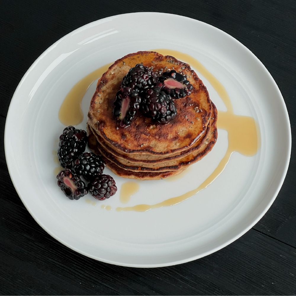 Stack of golden-brown pancakes topped with blackberries and maple syrup on a white plate