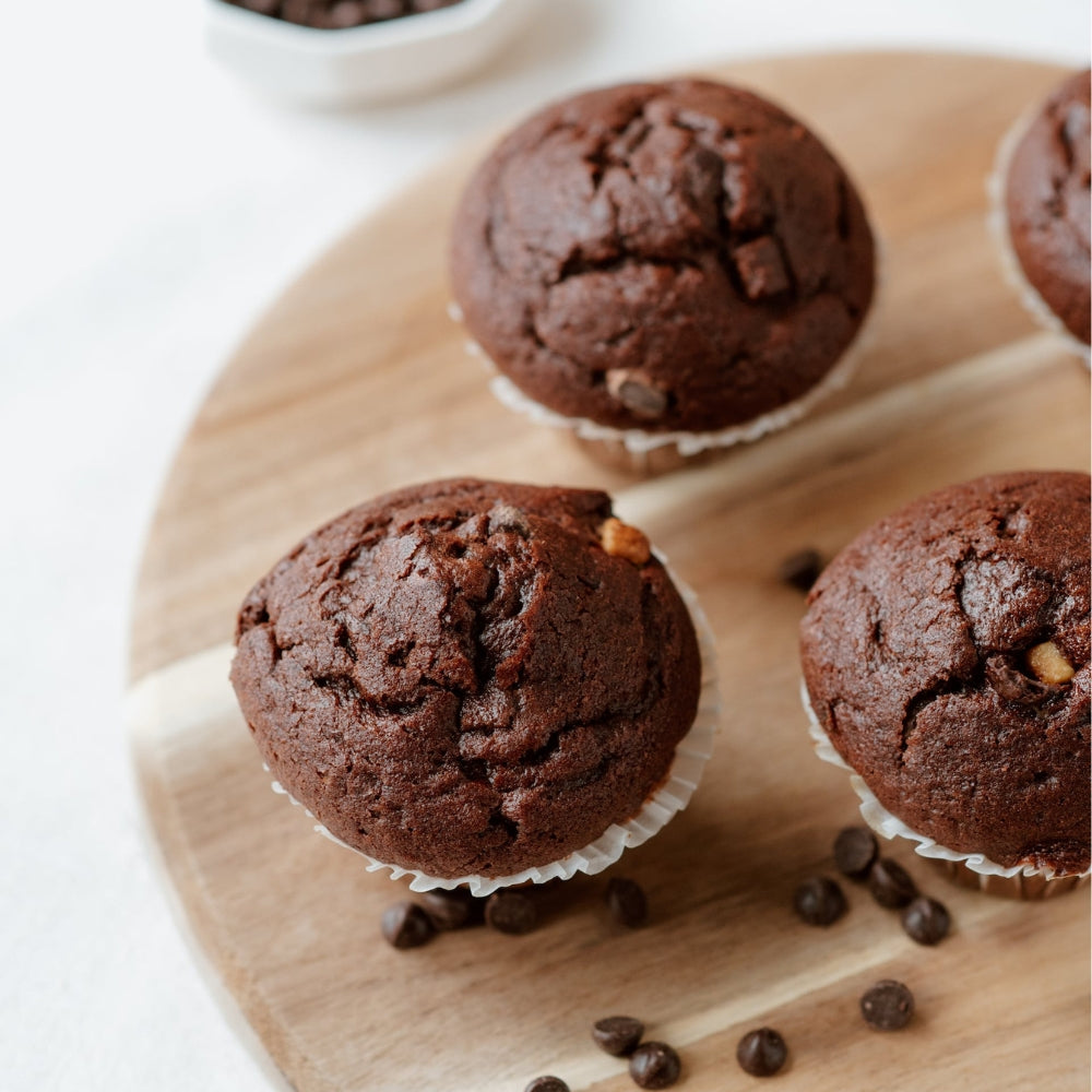 Three chocolate muffins with chocolate chips on a round wooden board