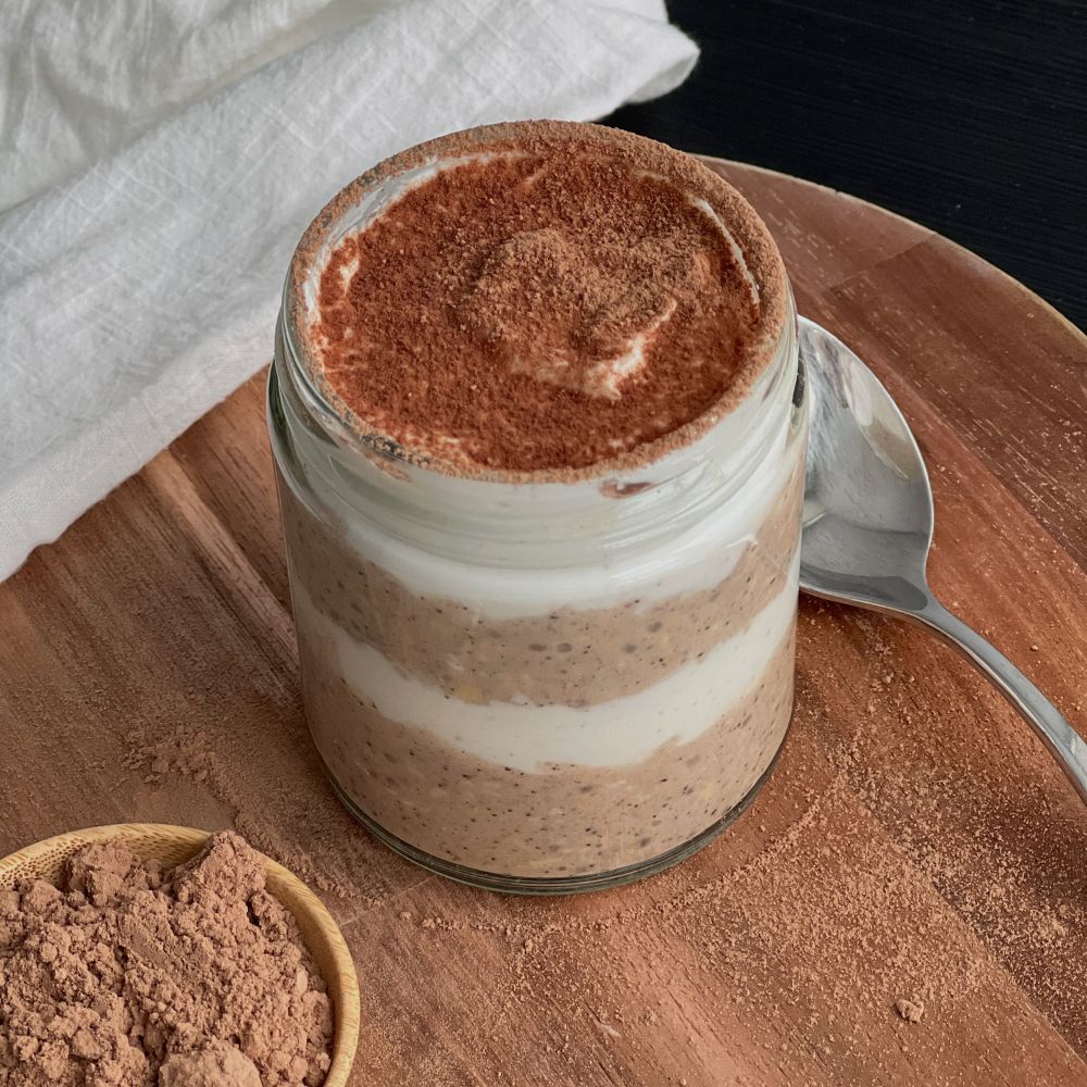 Layered chocolate and vanilla chia pudding in a small glass jar, cocoa powder dusted on top, spoon beside jar