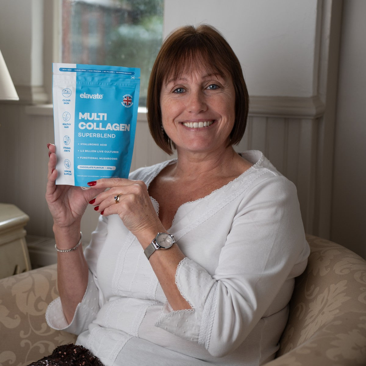 Smiling woman seated holding blue pouch labeled MULTI COLLAGEN SUPERBLEND by elavate