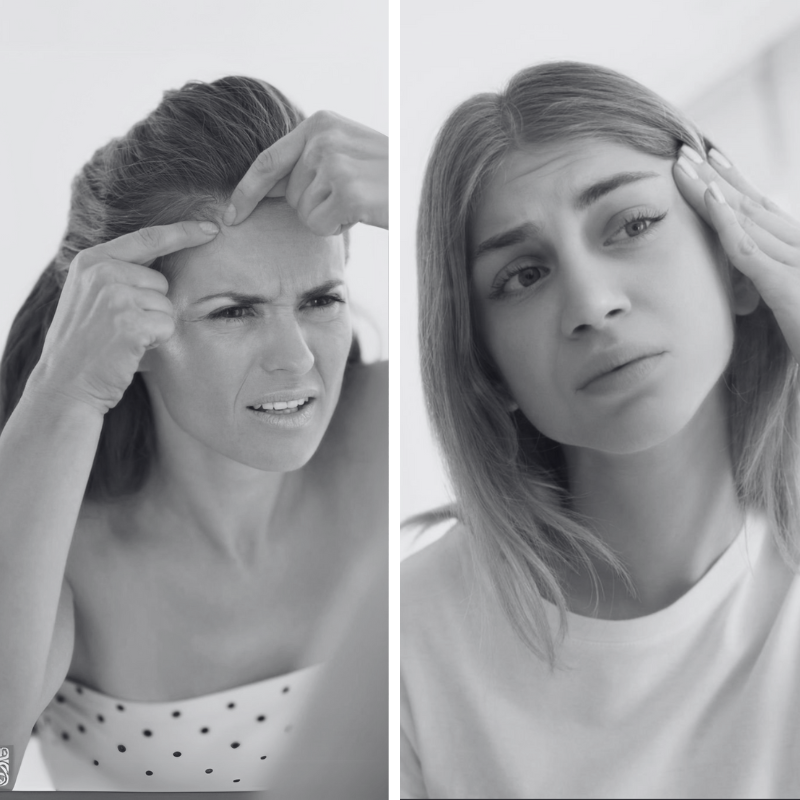 Two women examining their foreheads in a mirror, frowning as they check for wrinkles and blemishes